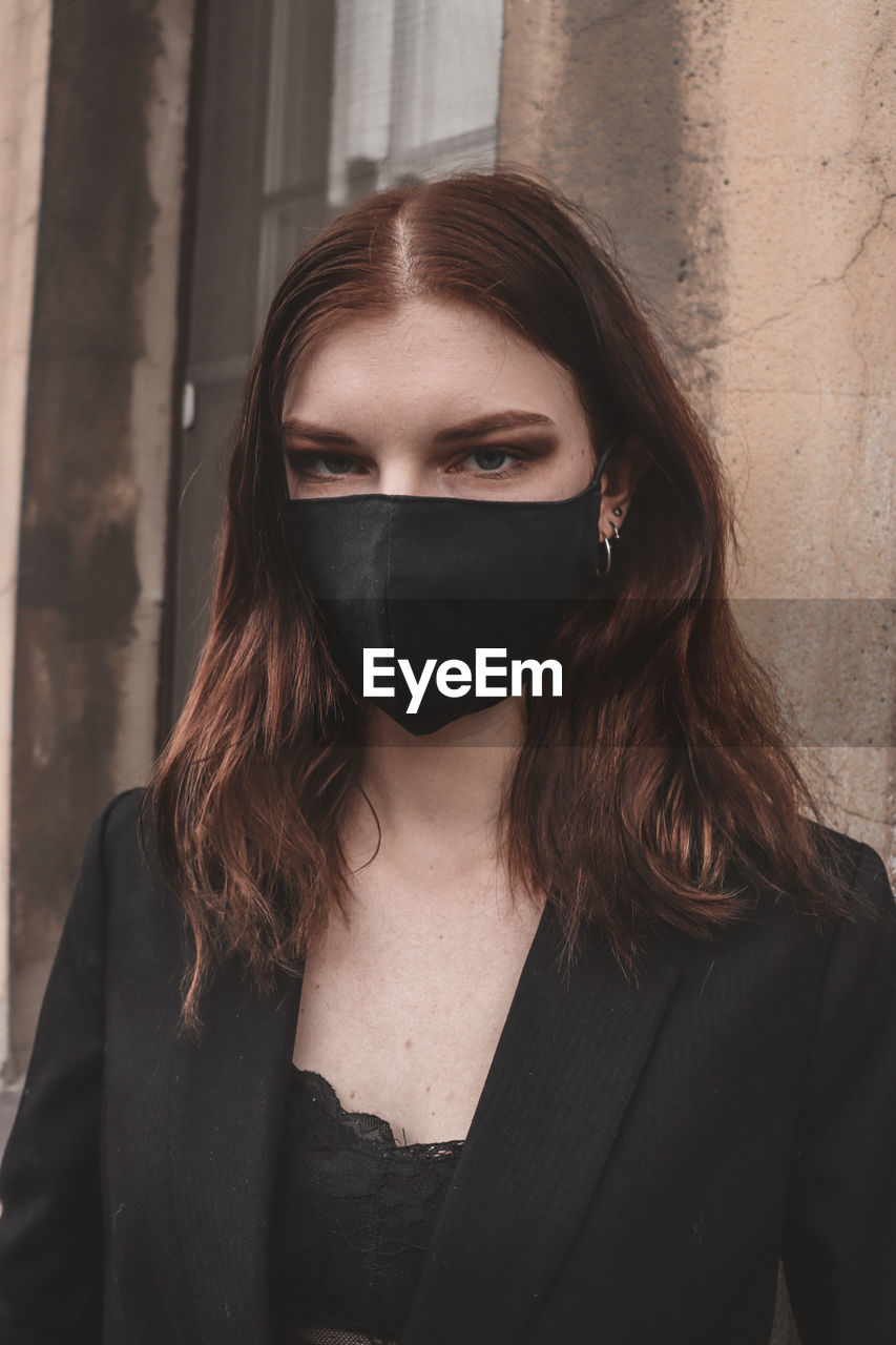 Portrait of woman wearing pollution mask while standing against wall