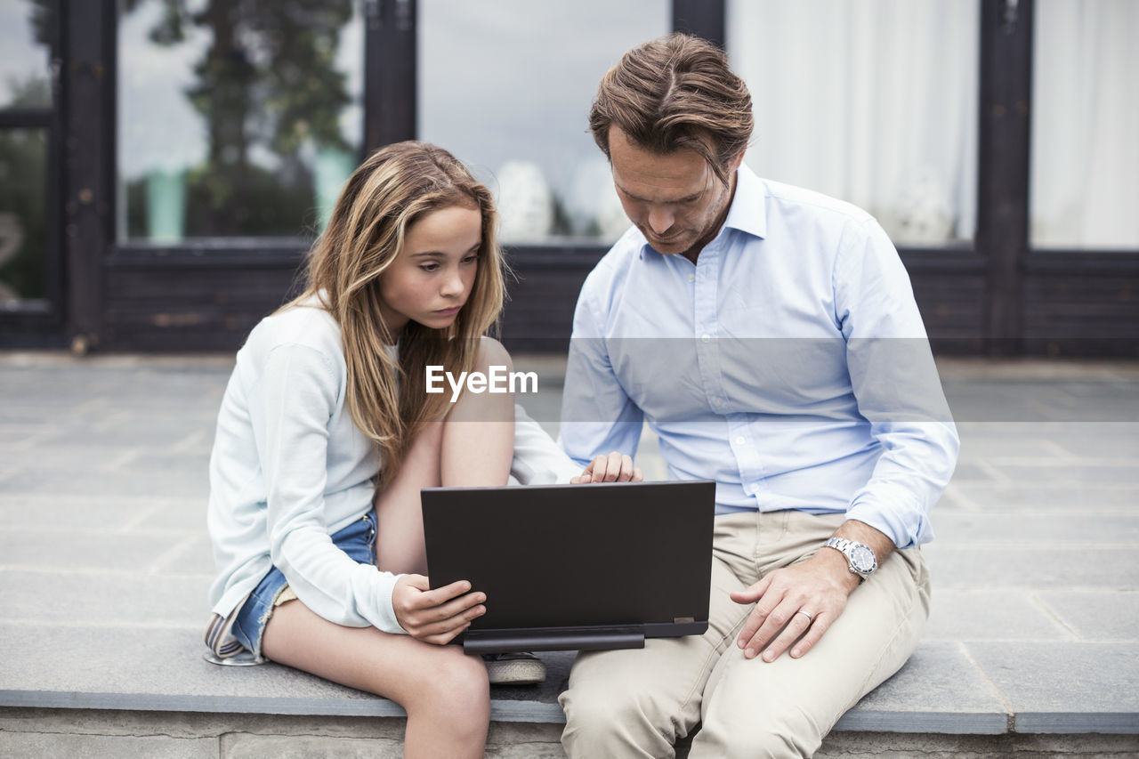 Father and daughter using laptop together at porch