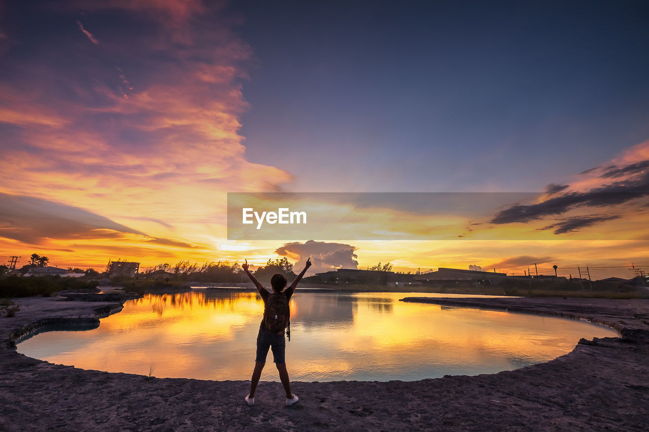 WOMAN STANDING BY LAKE DURING SUNSET