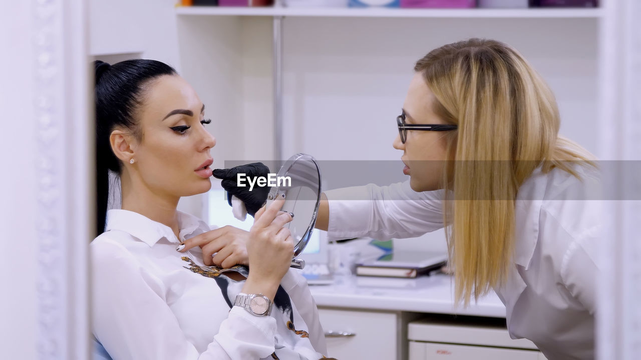 Clinic, cosmetology room, the doctor shows the patient a lip zone for injection of hyaluronic acid