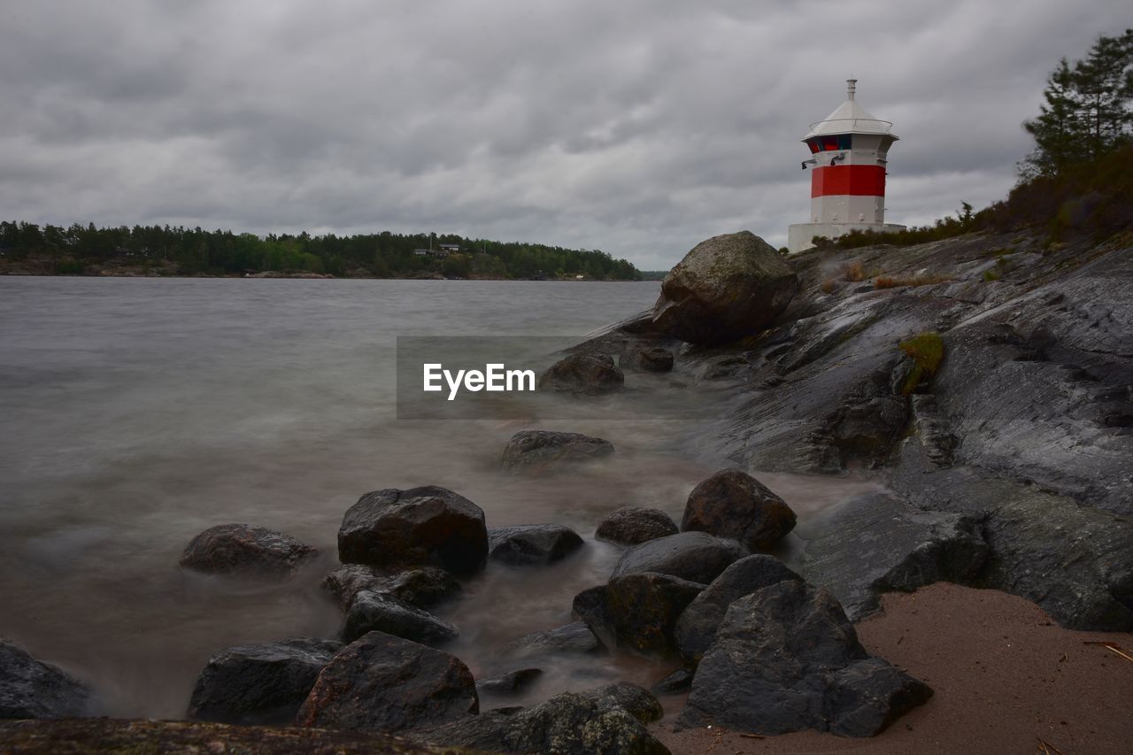 LIGHTHOUSE AMIDST ROCKS AND SEA AGAINST SKY