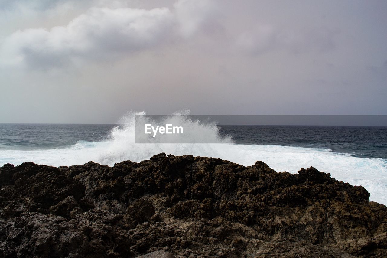 SCENIC VIEW OF WAVES BREAKING AGAINST ROCKS
