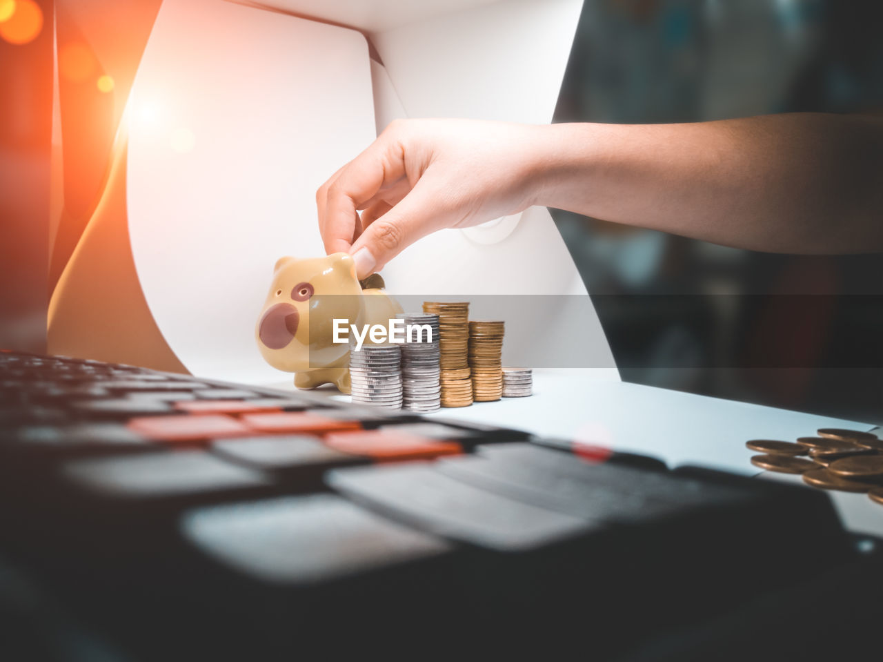 Cropped hand of woman putting coin in piggy bank over table