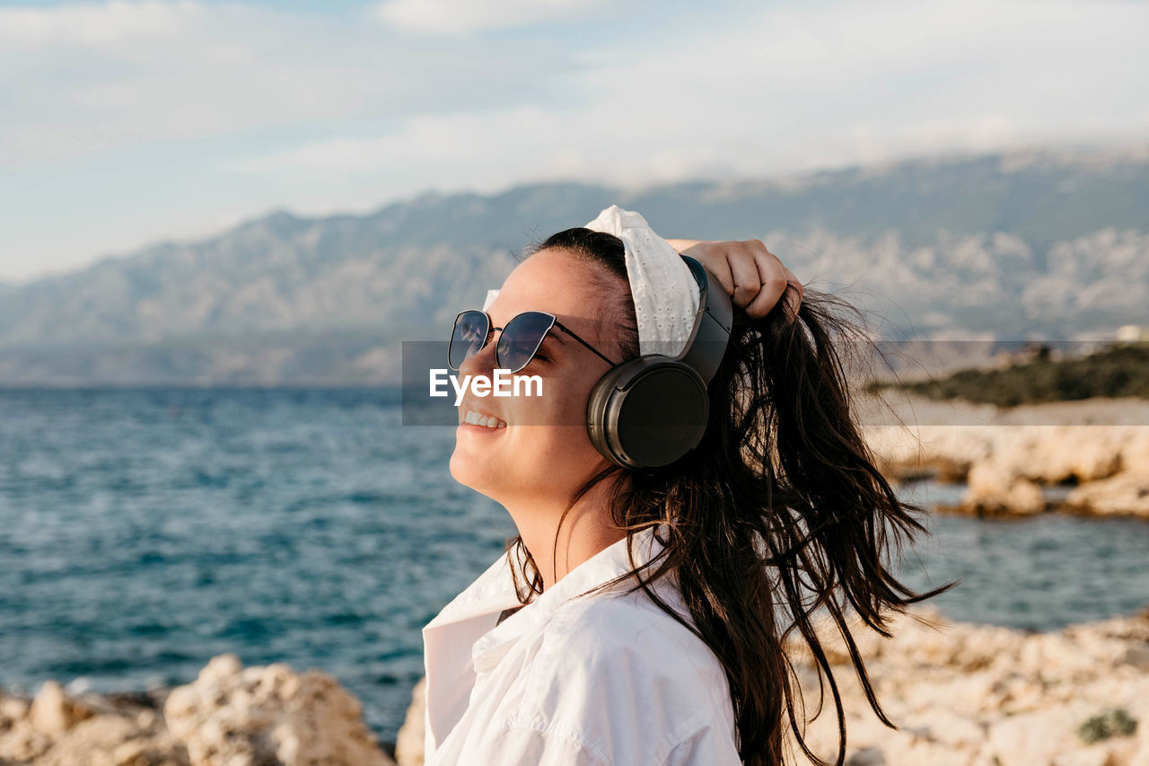 Side view of young woman in white shirt listening to music on headphones. summer, beach, lifestyle.