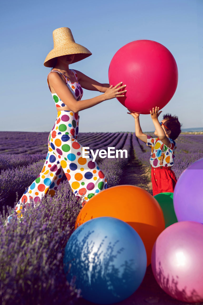 balloon, multi colored, women, hat, nature, adult, toy, one person, clothing, female, sky, blue, fun, celebration, helium balloon, happiness, child, summer, holiday, emotion, land, leisure activity, childhood, holding, outdoors, young adult, sun hat, event, day, lifestyles, full length, party, dress