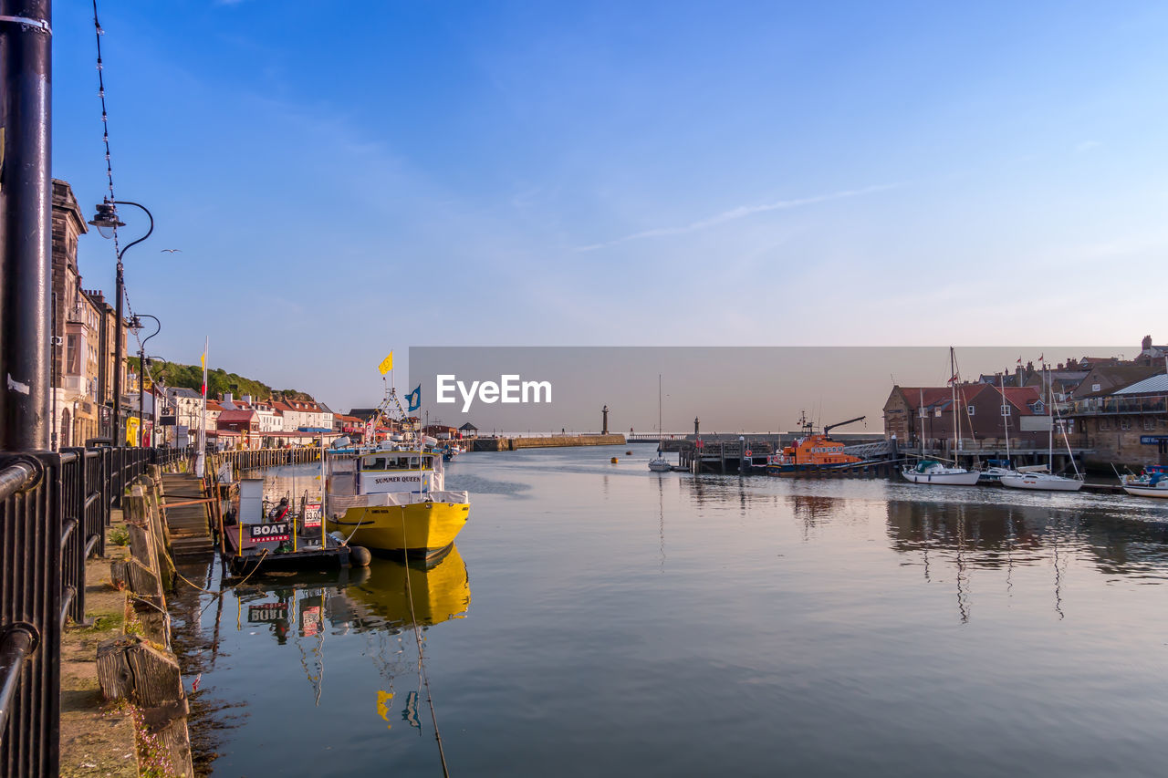 Sailboats moored on river by buildings in city against sky