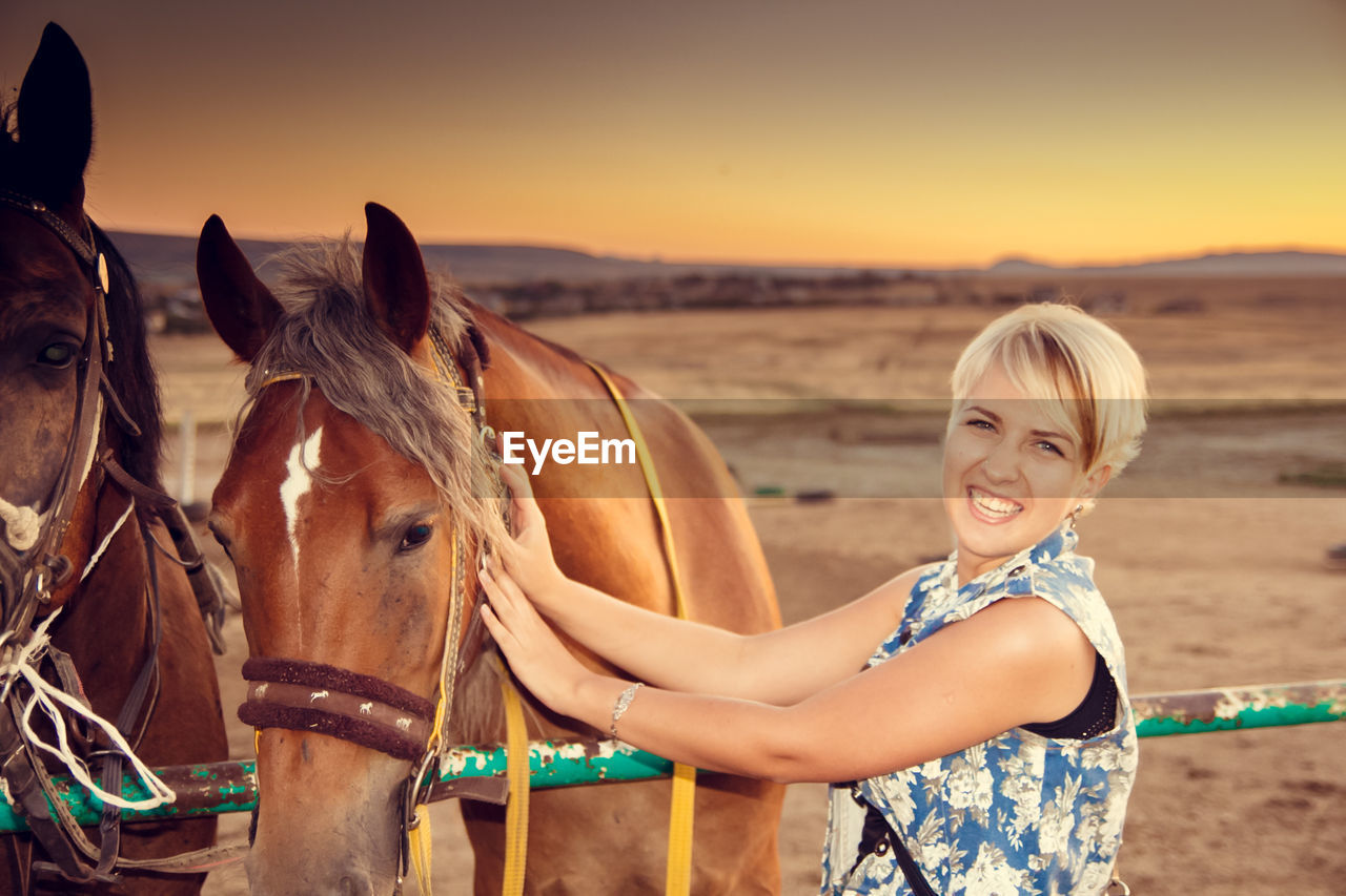 Portrait of smiling young woman holding brown horse on field