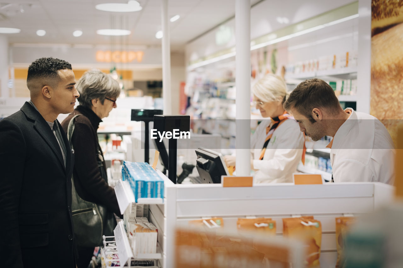 Customers and pharmacists standing at checkout in medical store