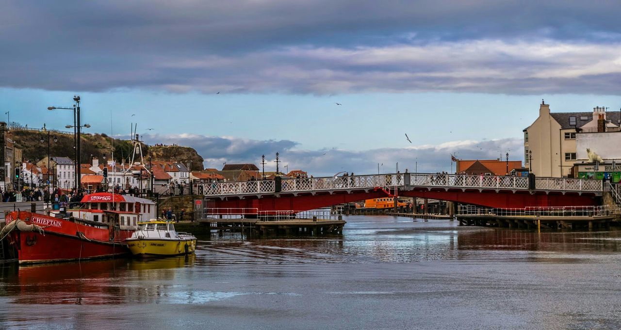 Boats moored in river near bridge against cloudy sky