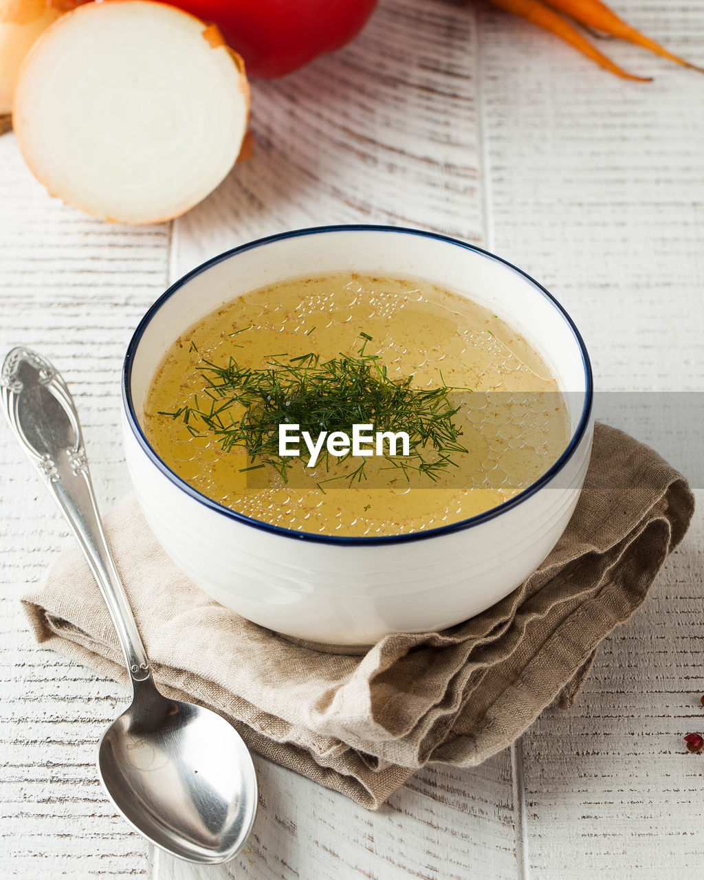 Healthy bone broth in a bowl with dill on a light wooden background.