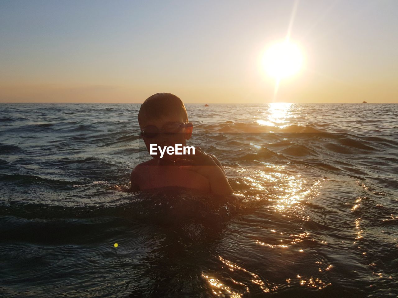 Portrait of boy swimming in sea against sky during sunset