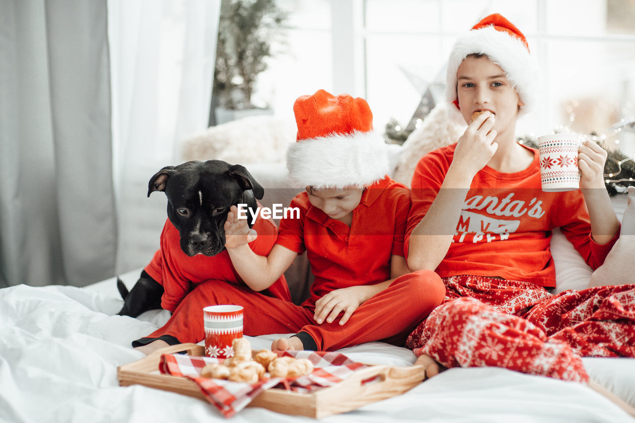 Cute kids drinking hot chocolate while sitting on bed with dog at home