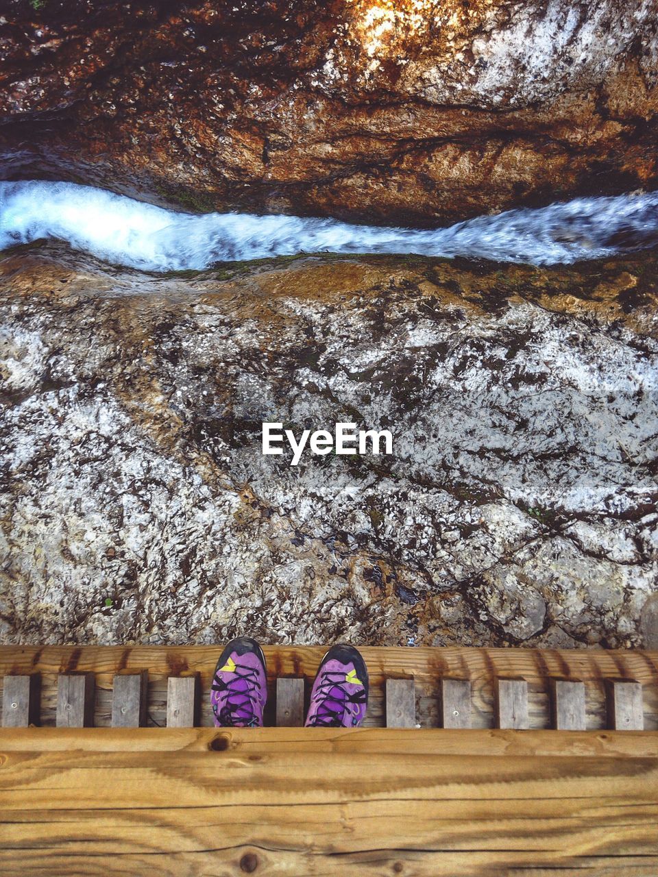 Low section of man standing on the wooden bridge above water stream