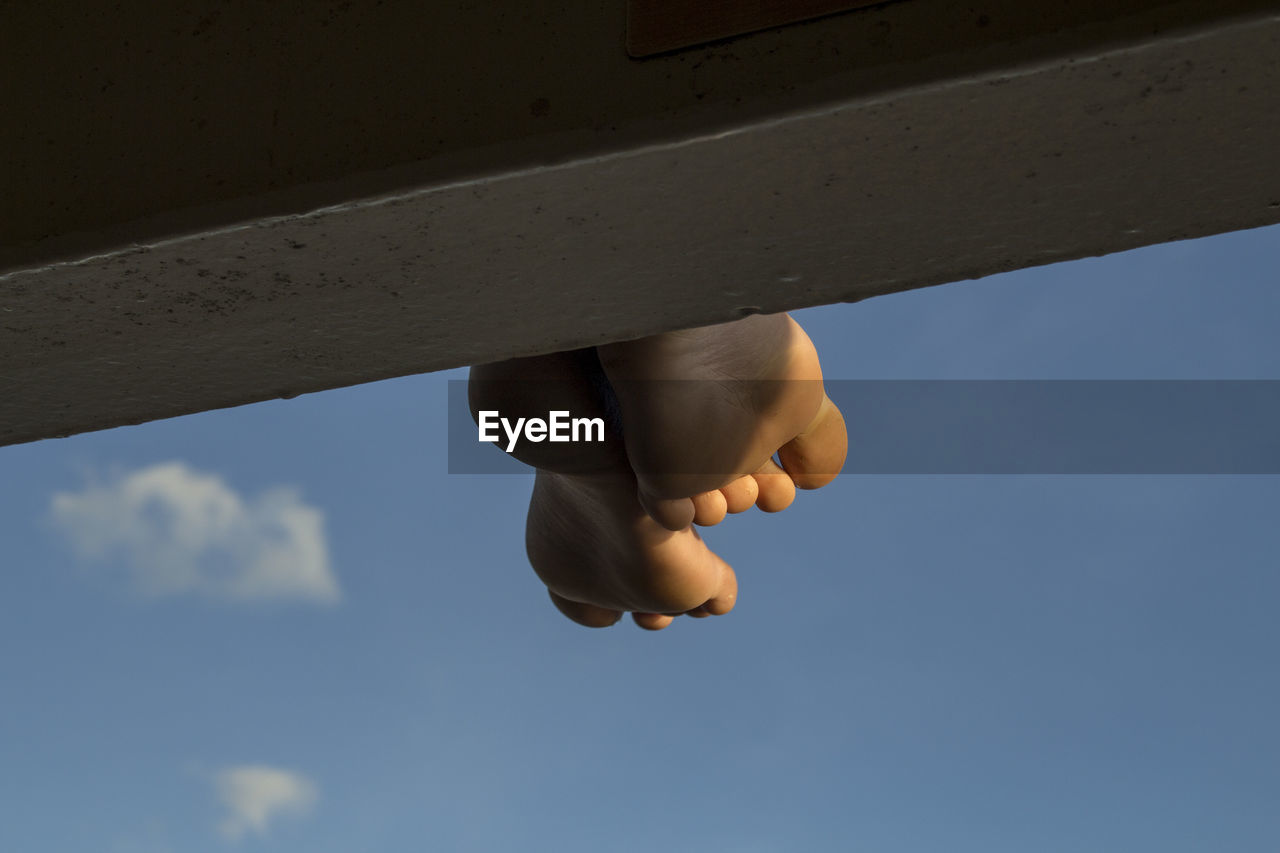 Close-up low angle view of barefeet against sky