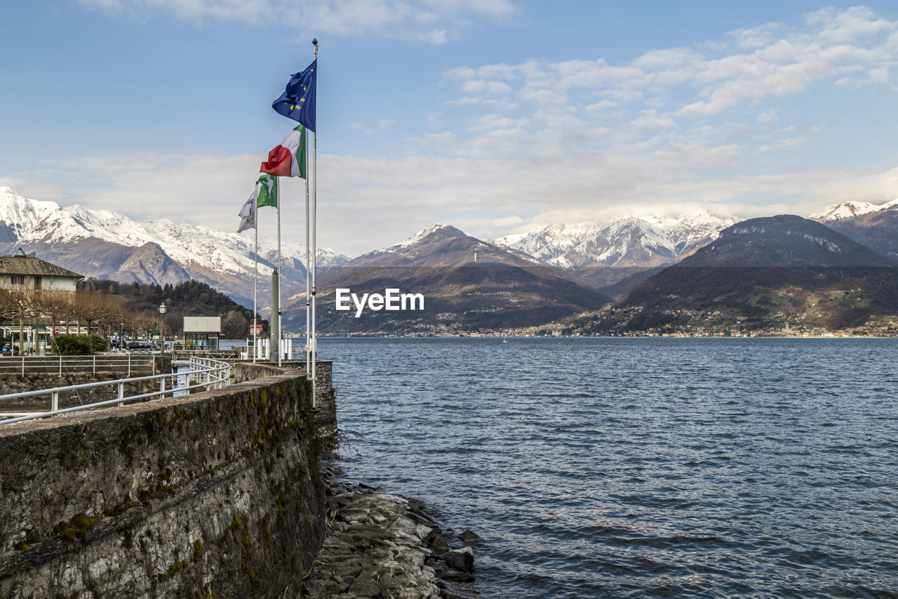 The port of colico with the waving flags of italy and europe with the snow capped alps 