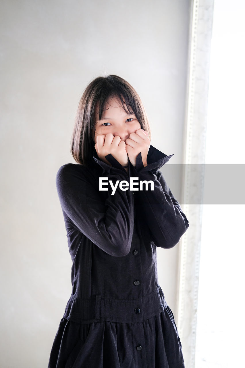 Portrait of girl covering mouth standing against wall