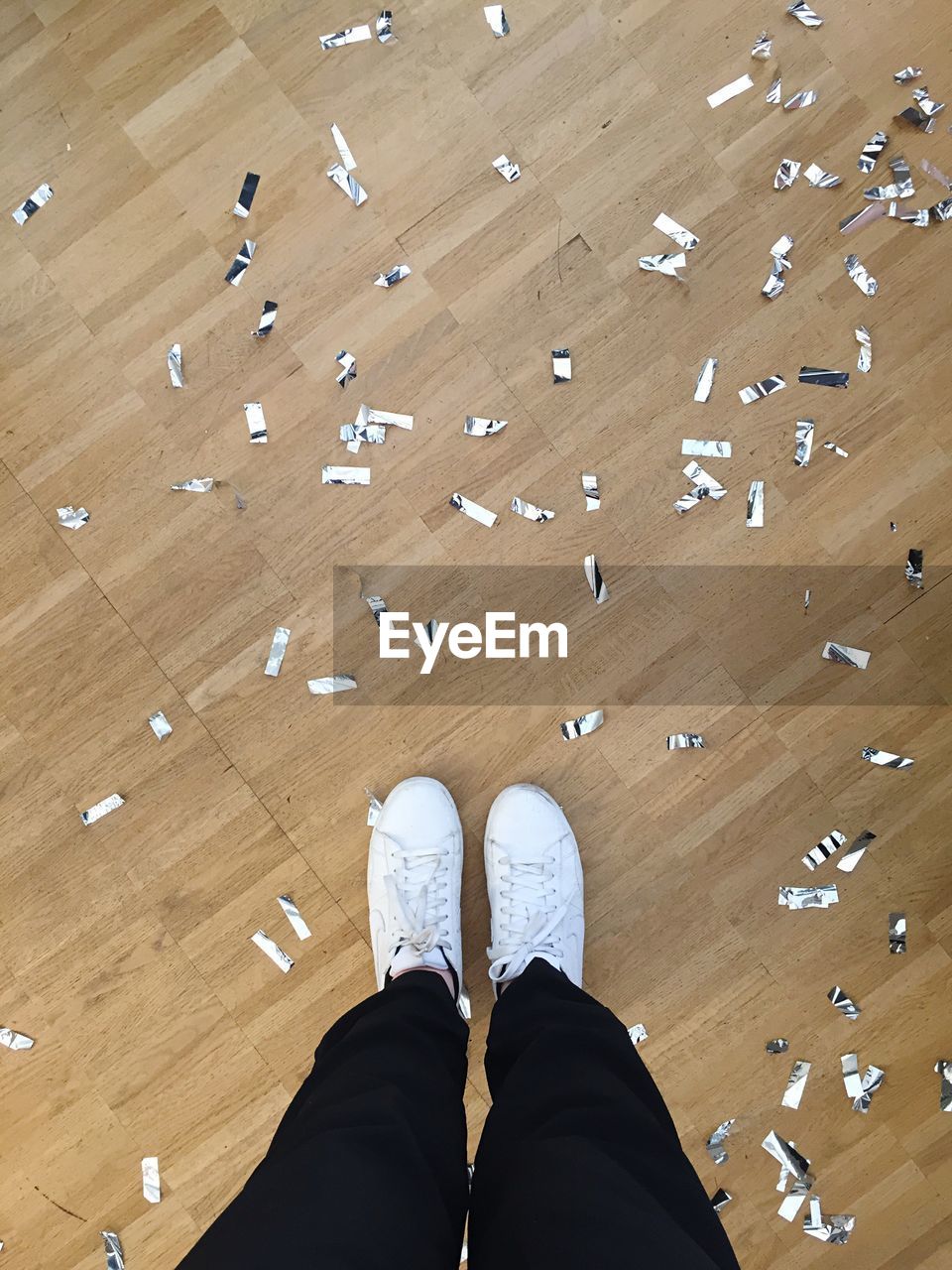 Low section of person standing by confetti on hardwood floor