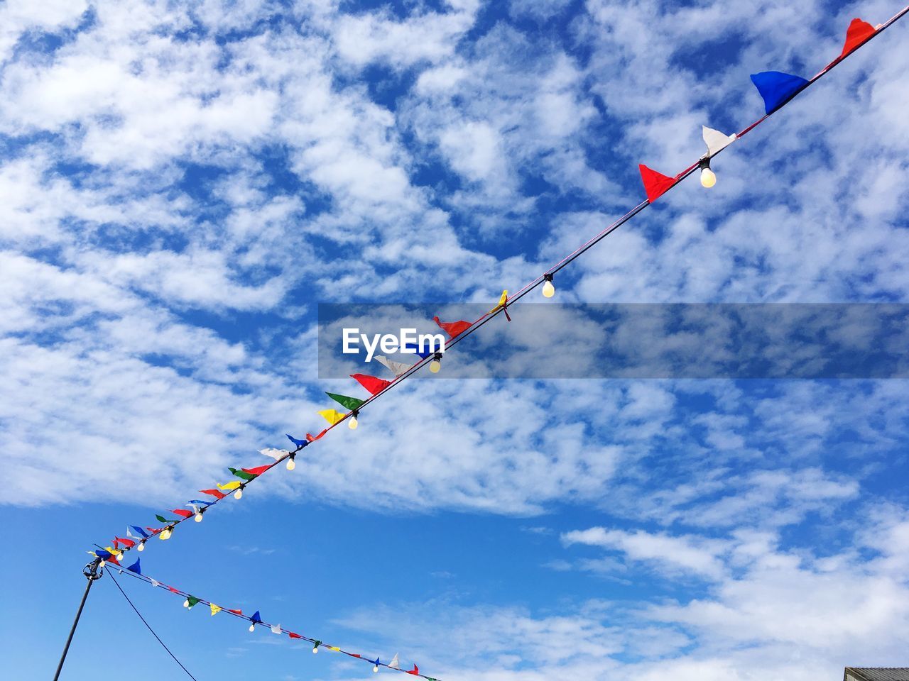 Low angle view of buntings and illuminated light bulbs hanging against sky