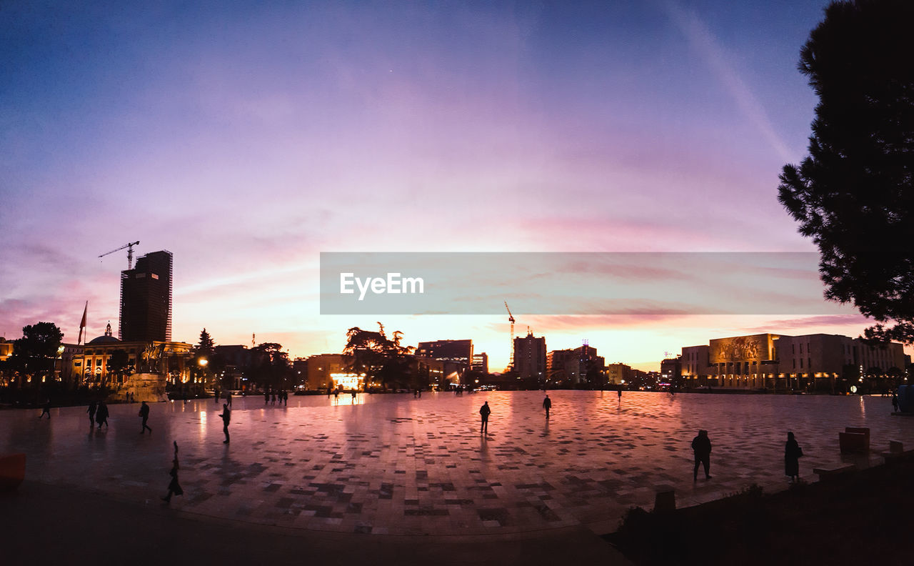 SILHOUETTE BUILDINGS BY RIVER AGAINST SKY AT SUNSET