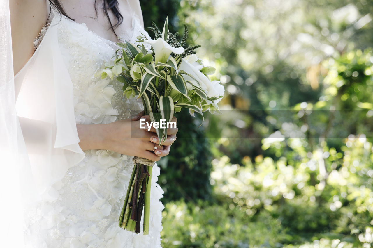 Midsection of bride holding white flowers at park