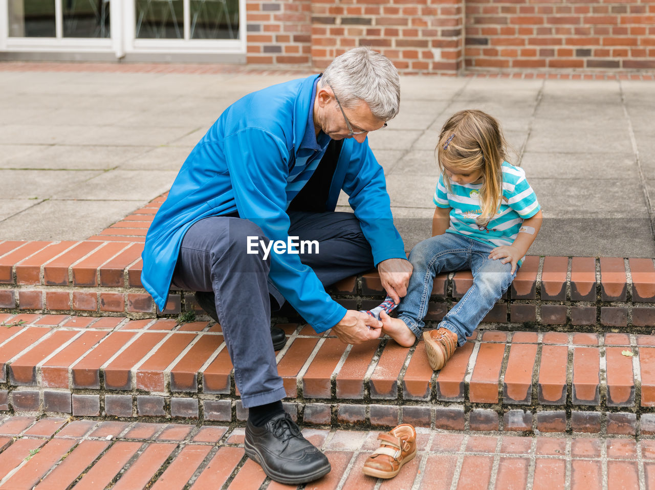 Full length of grandfather assisting girl in wearing sock outdoors