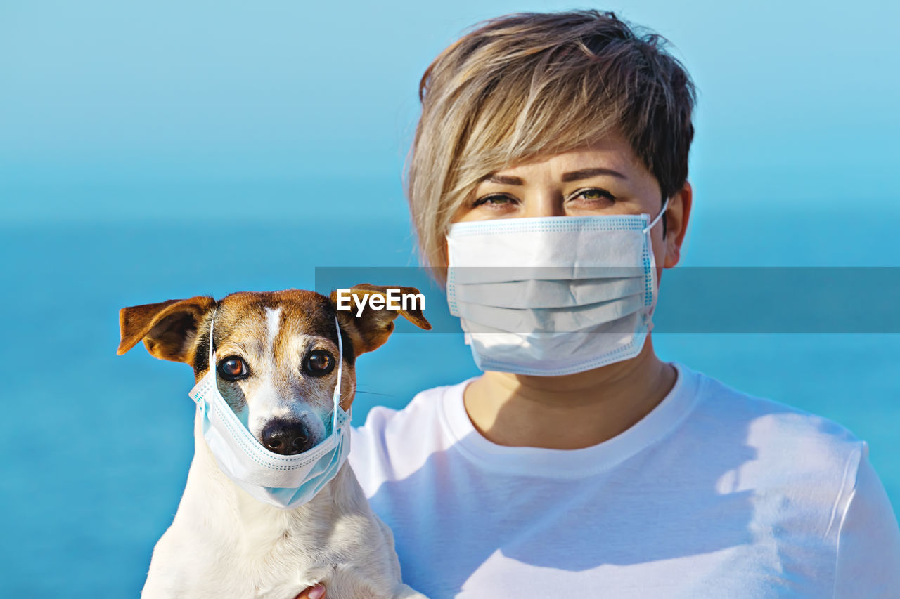Portrait of dog and woman wearing surgical masks against sea