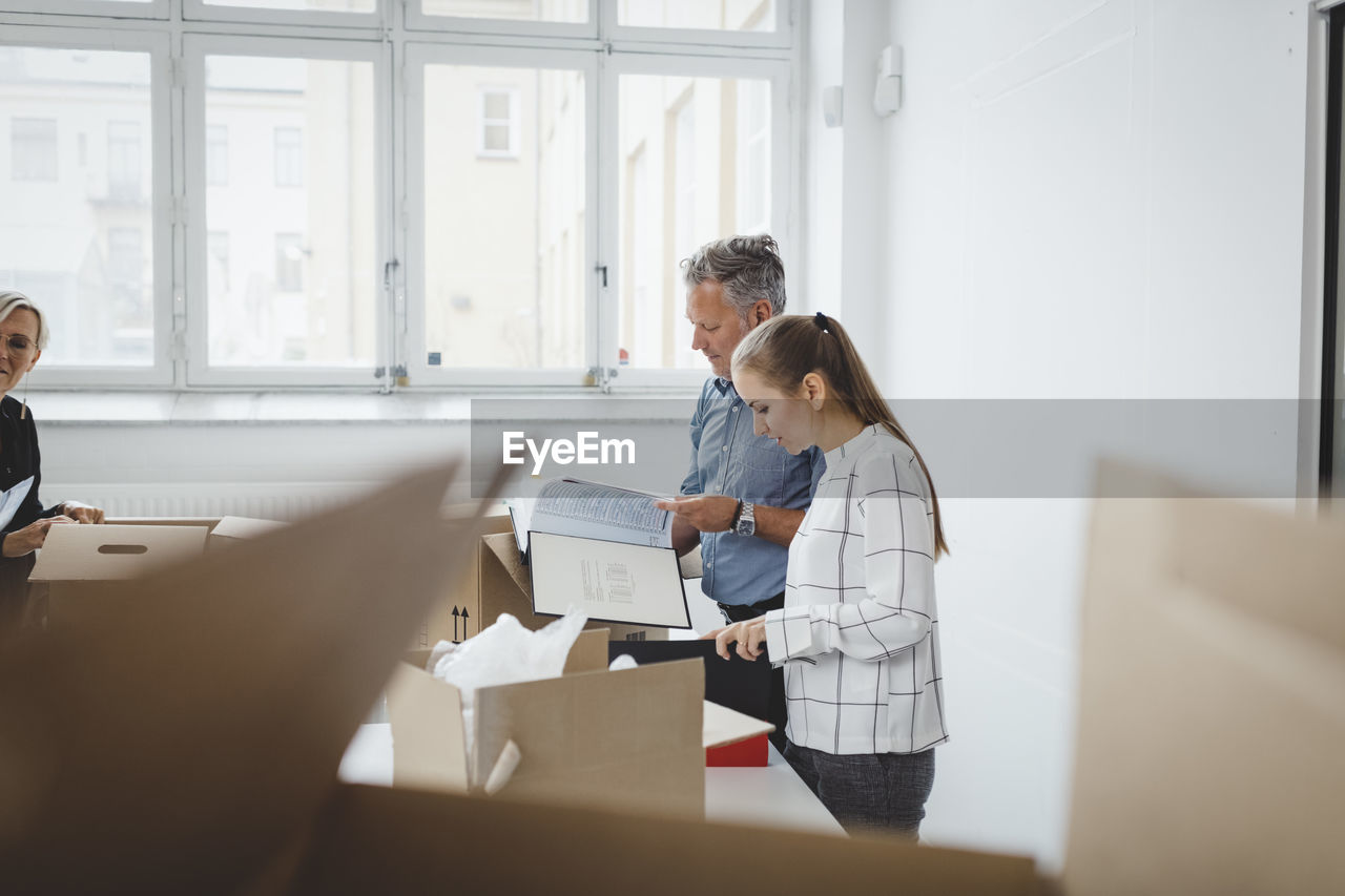 Business people unpacking moving boxes at table in new office