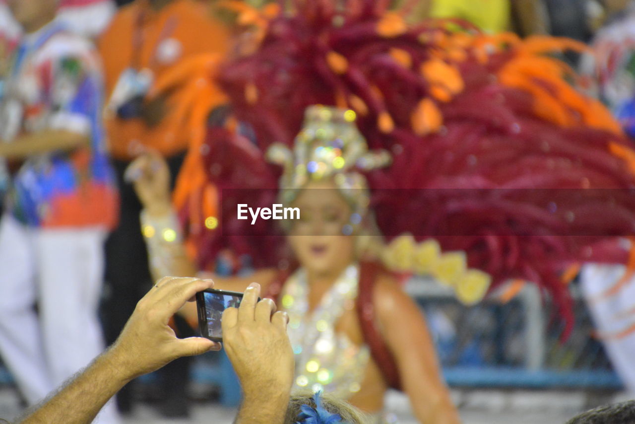 Cropped image of man photographing dancer at carnival