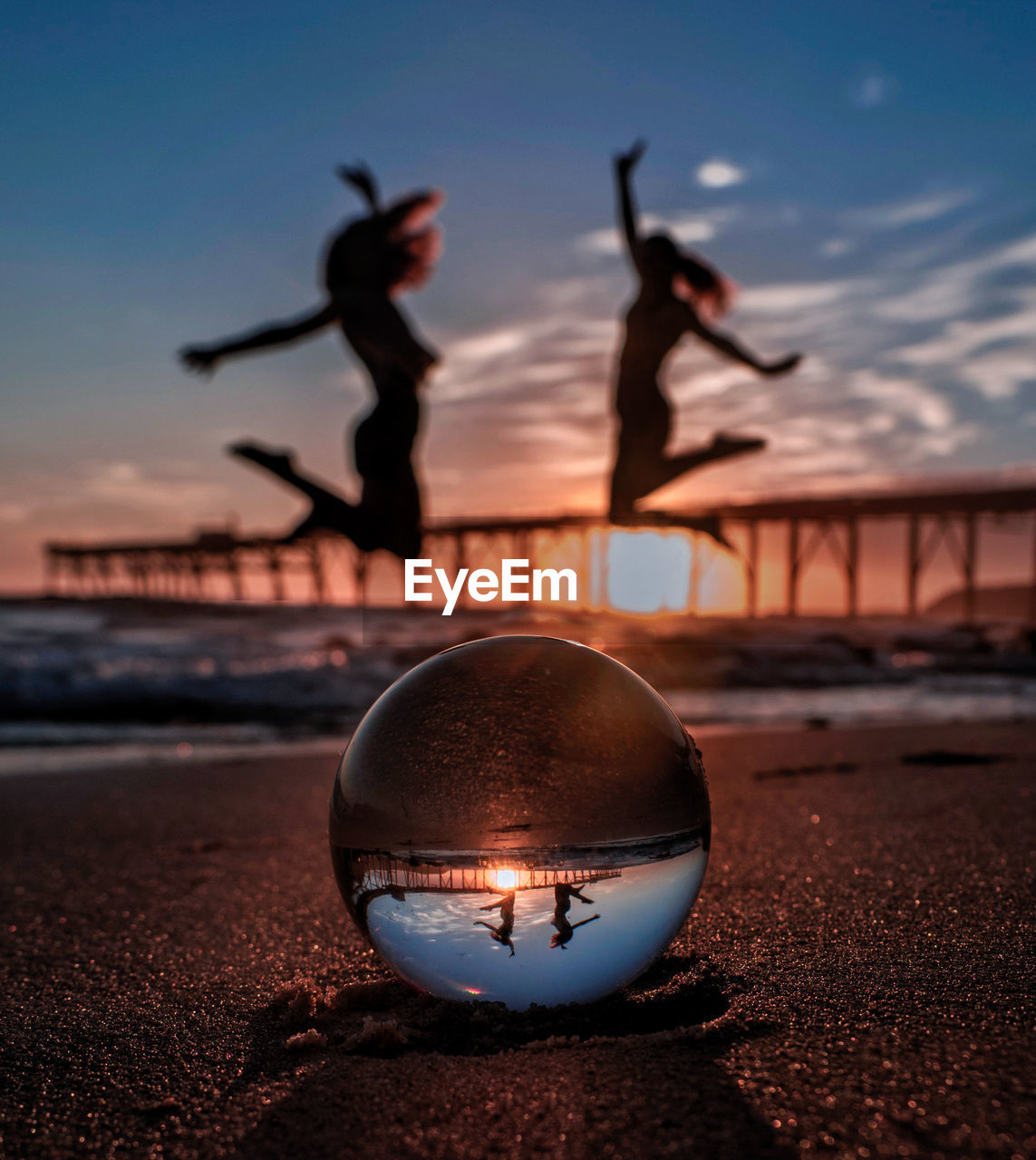 Upside down image of silhouette ball on beach against sky during sunset