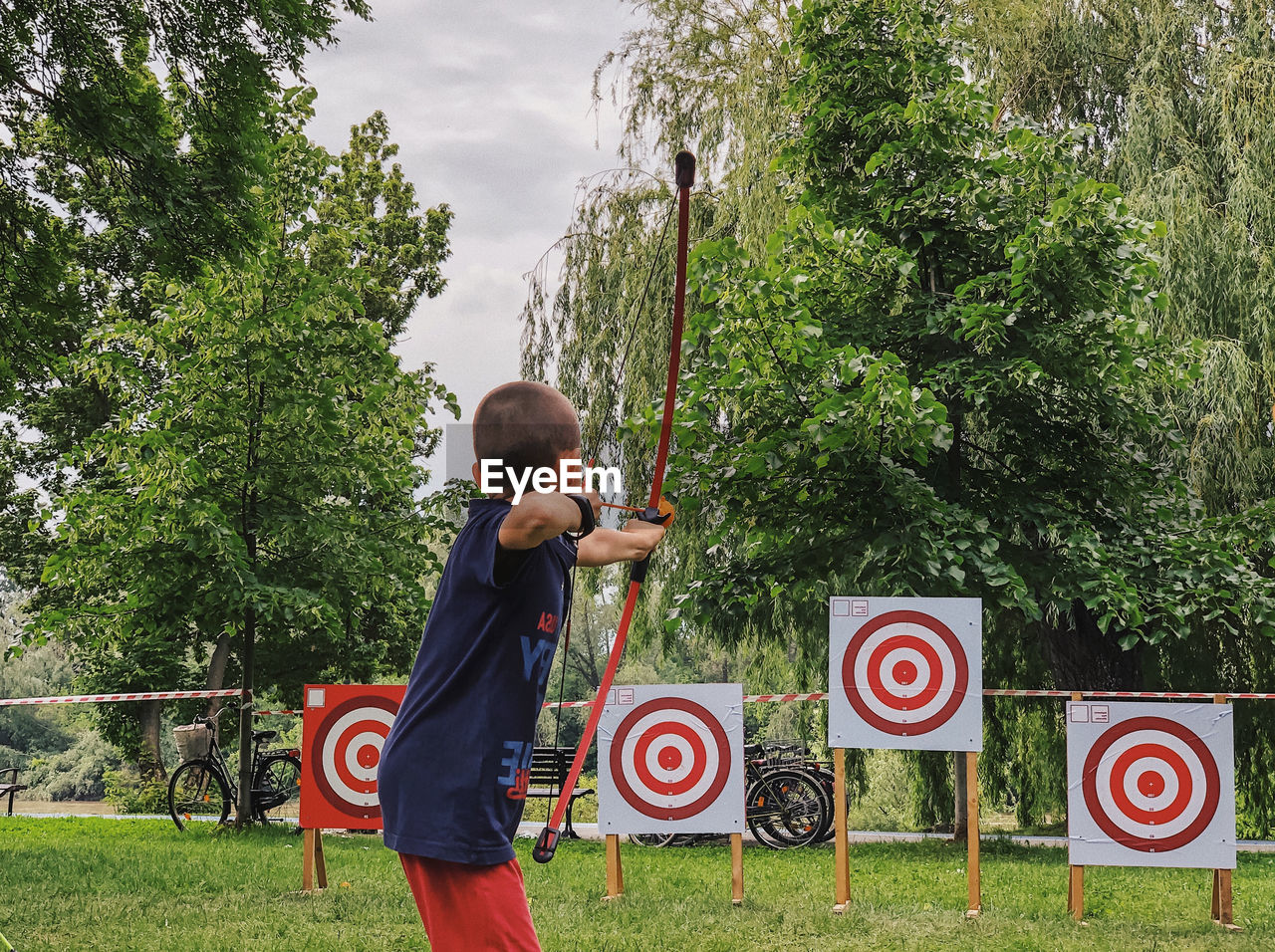 Side view of boy practicing archery against trees