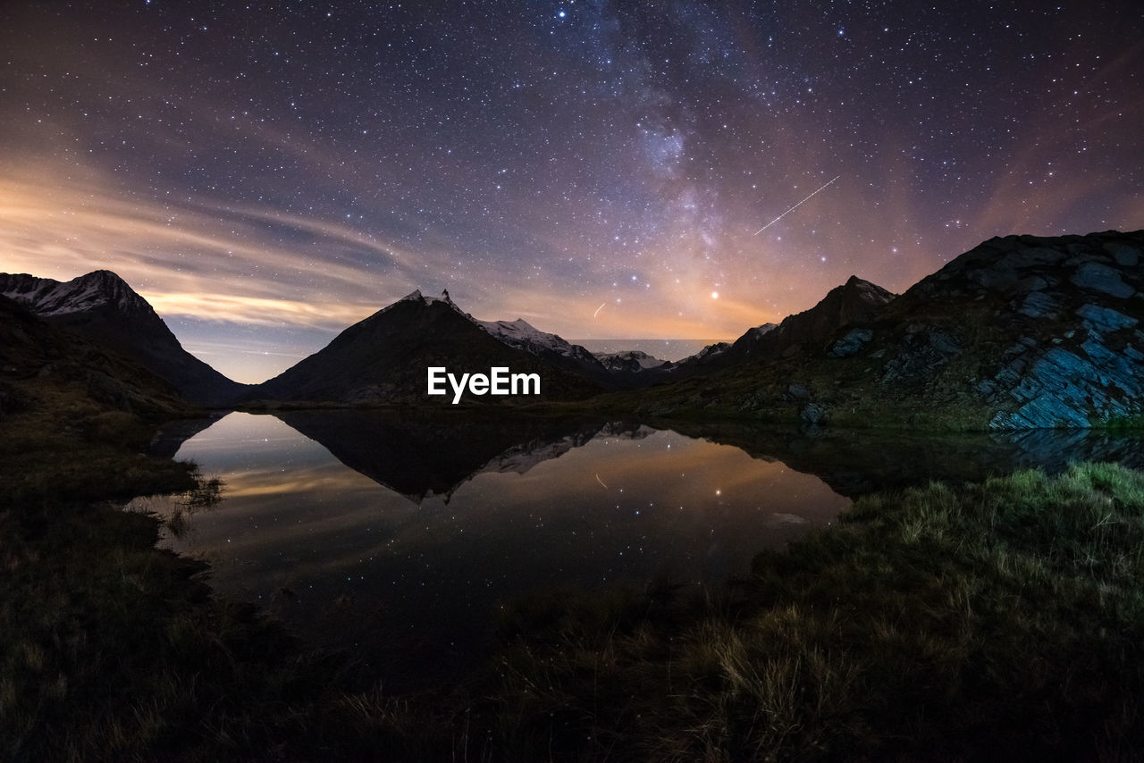 Scenic view of lake by mountains against sky at night
