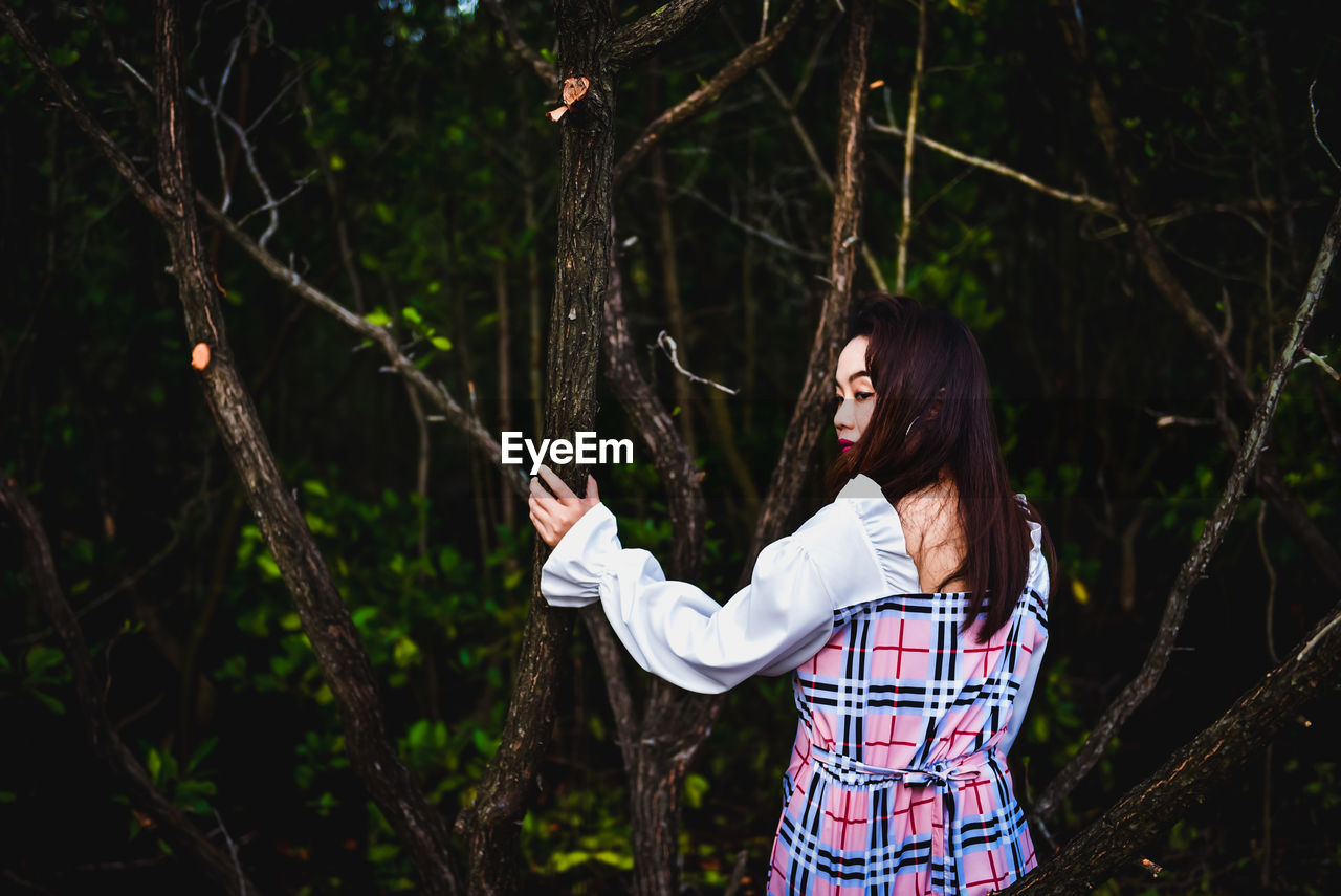 WOMAN WEARING HAT STANDING AGAINST TREES IN FOREST