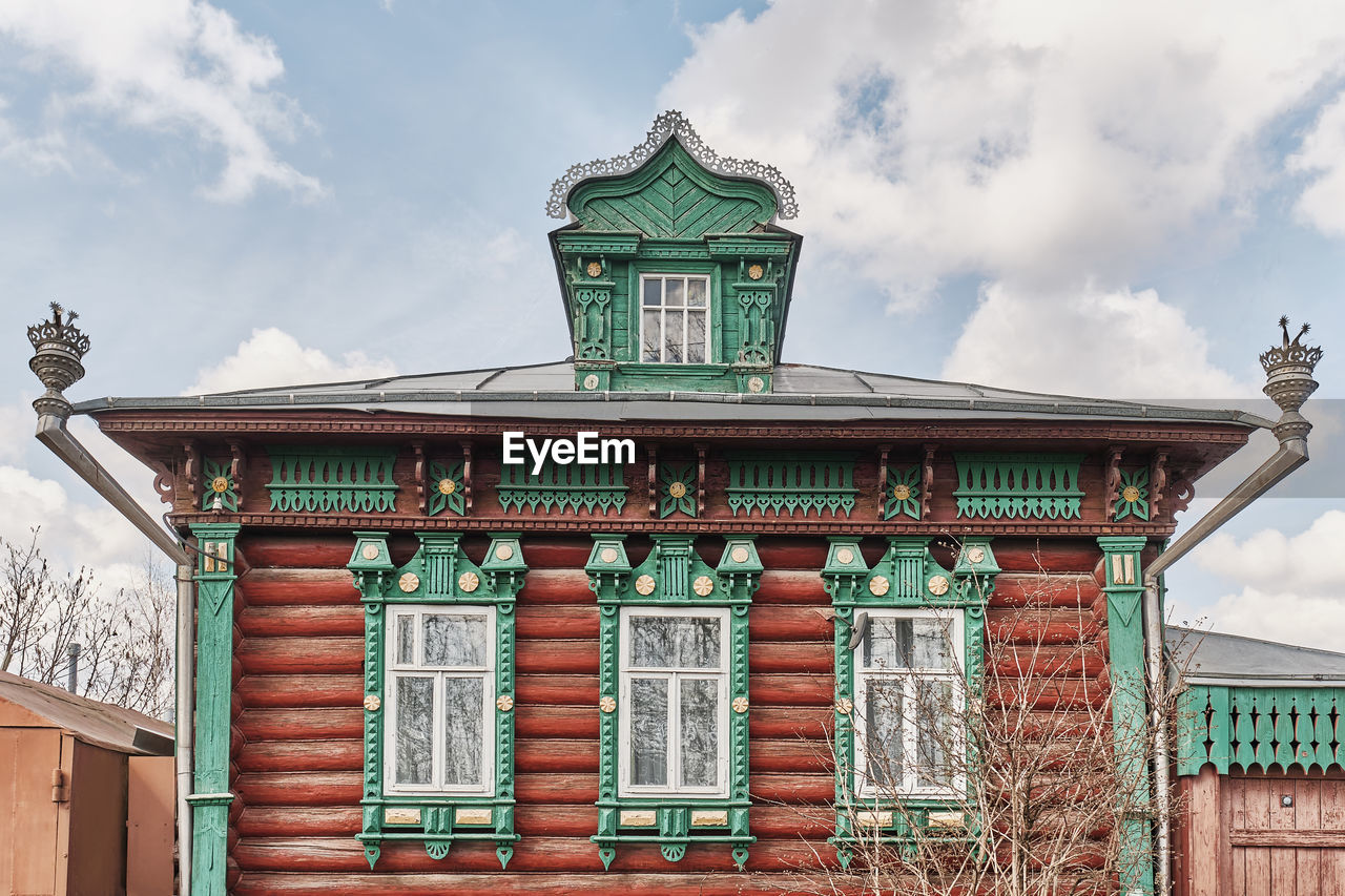 Facade of russian log house with dormer window on roof and carved wooden decorations