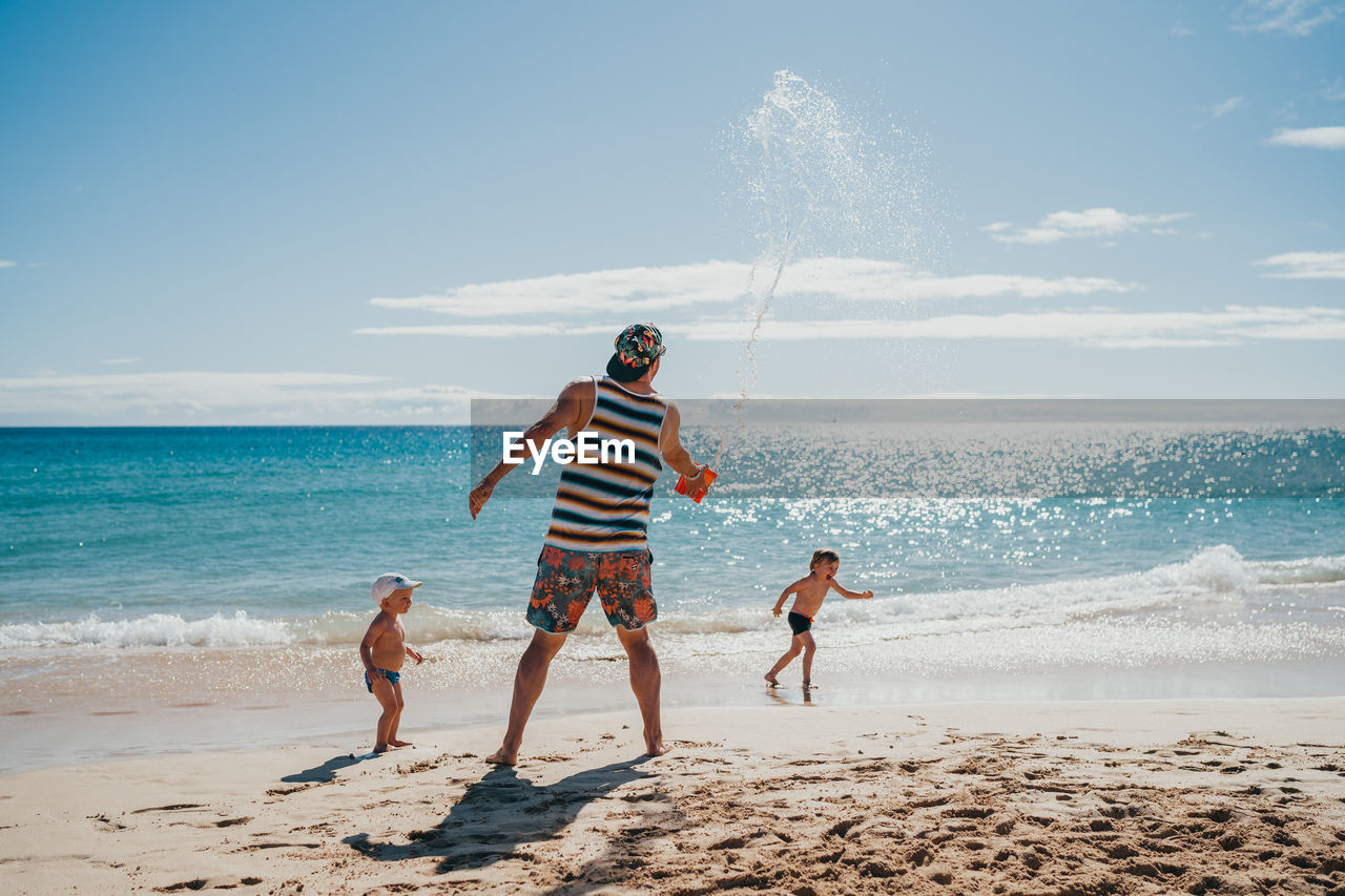 Kids playing with water at the beach with their dad on a sunny day