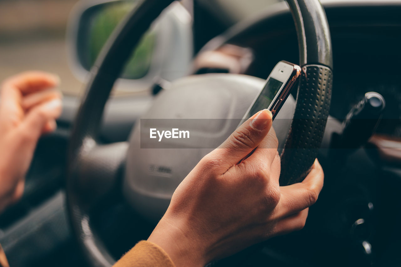 Cropped hands of woman using mobile phone while driving car