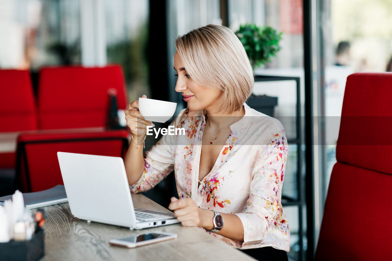 An elegant business woman drinks coffee, works in a cafe, uses a laptop, enjoys a break. 