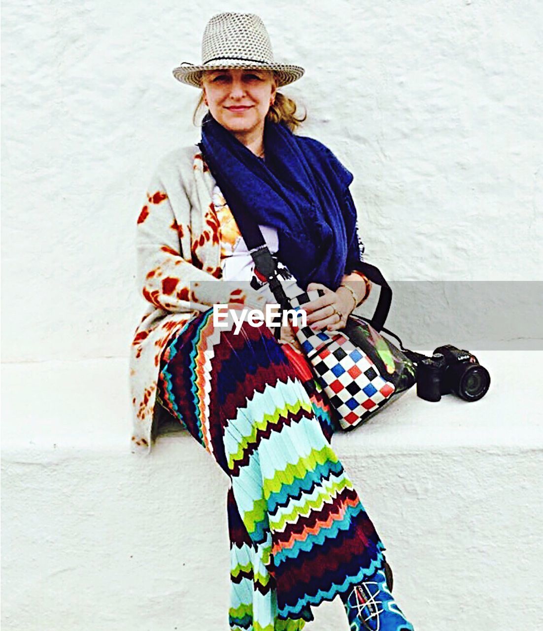 Portrait of woman wearing hat while sitting against wall