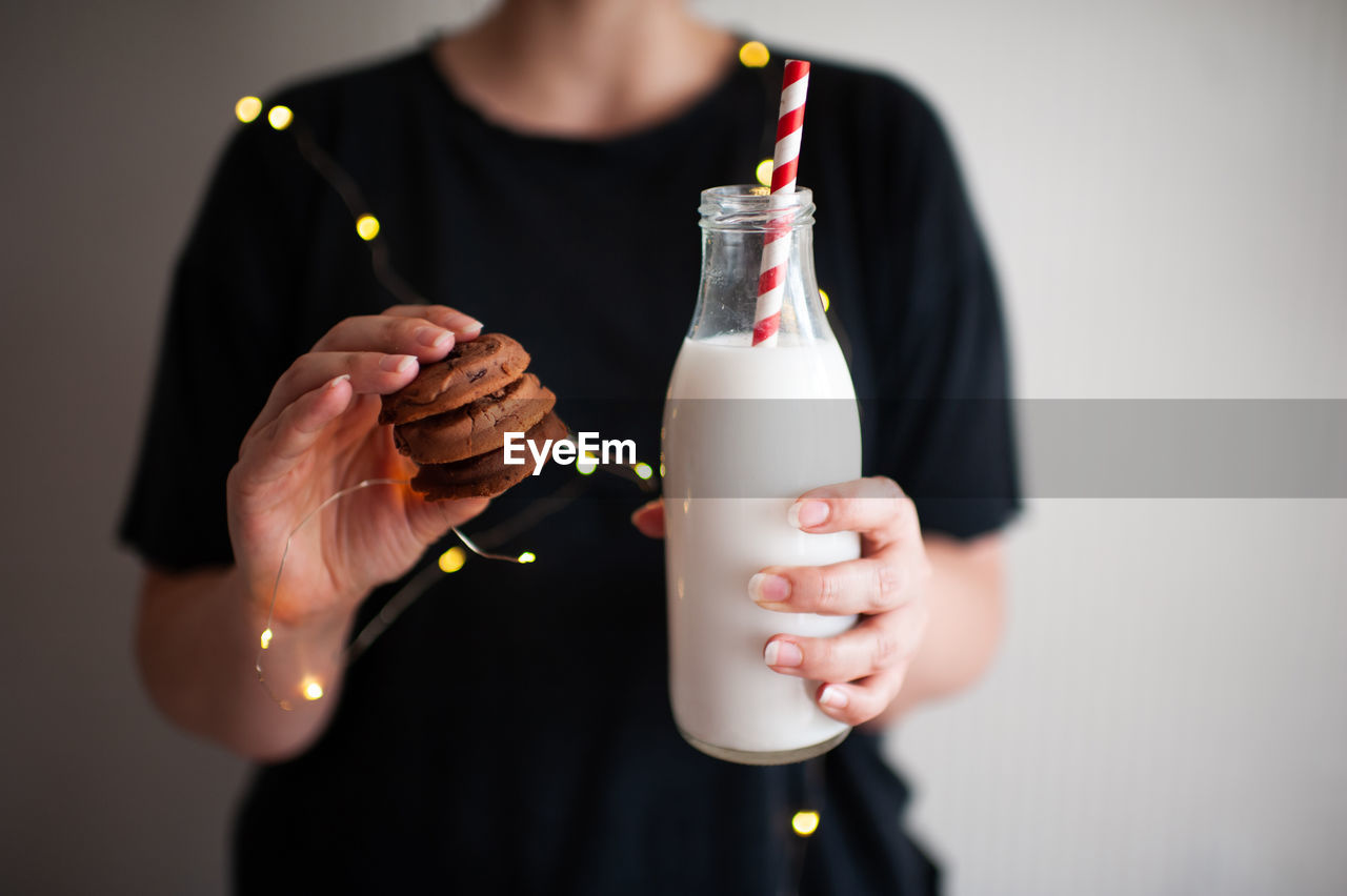 Woman holding tasty cookies and bottle of fresh milk over glowing lights close up. winter holiday