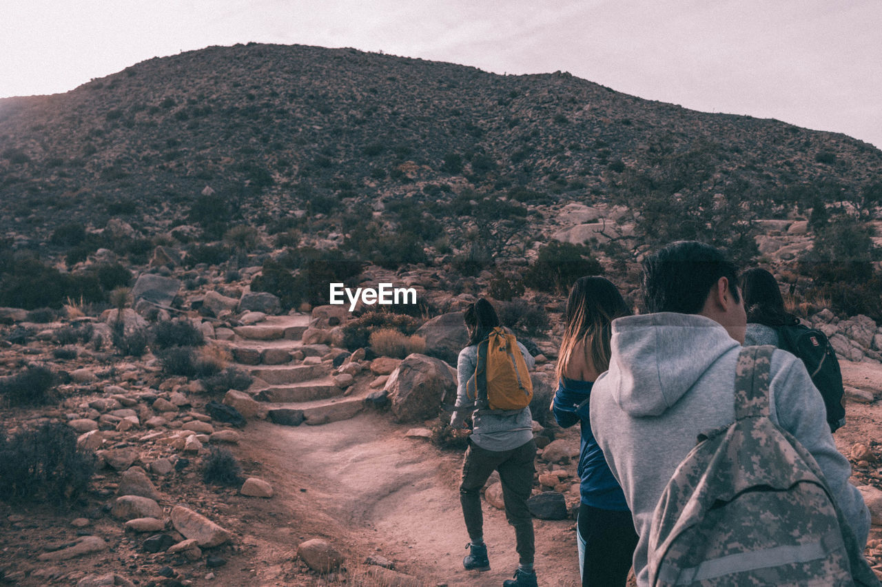 REAR VIEW OF PEOPLE WALKING ON LANDSCAPE AGAINST SKY