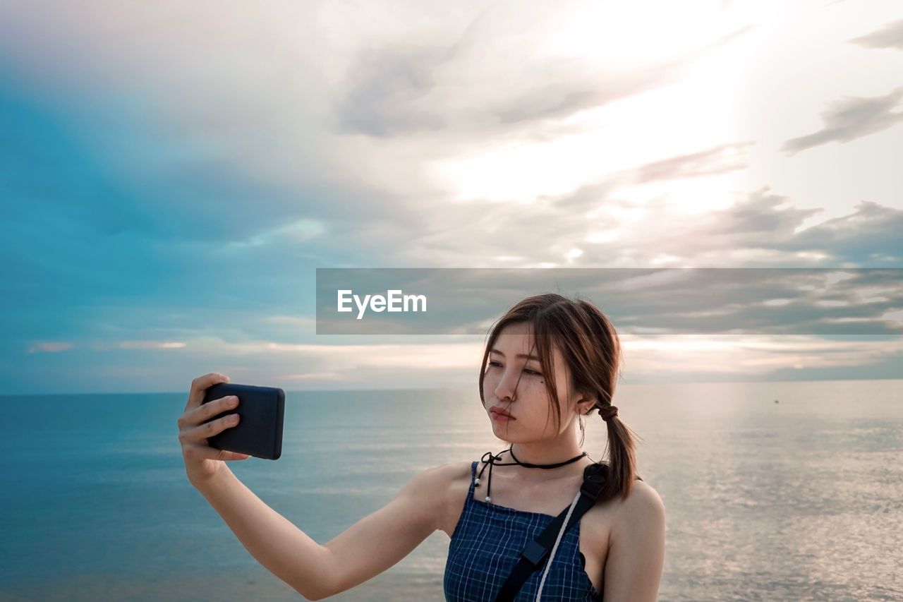 Young woman taking selfie while standing against sky