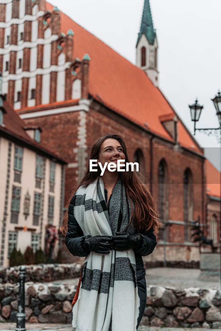 Young woman looking away while standing against building in city