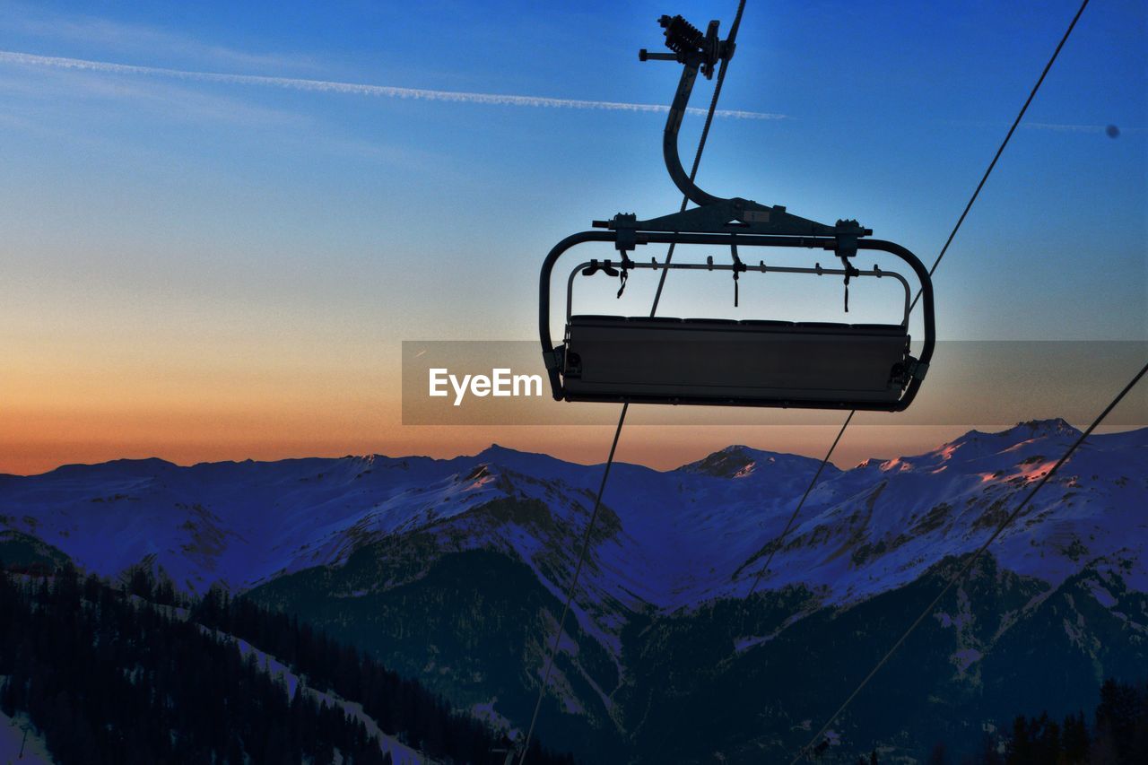 Overhead ski lift  against snowcapped mountains during sunset