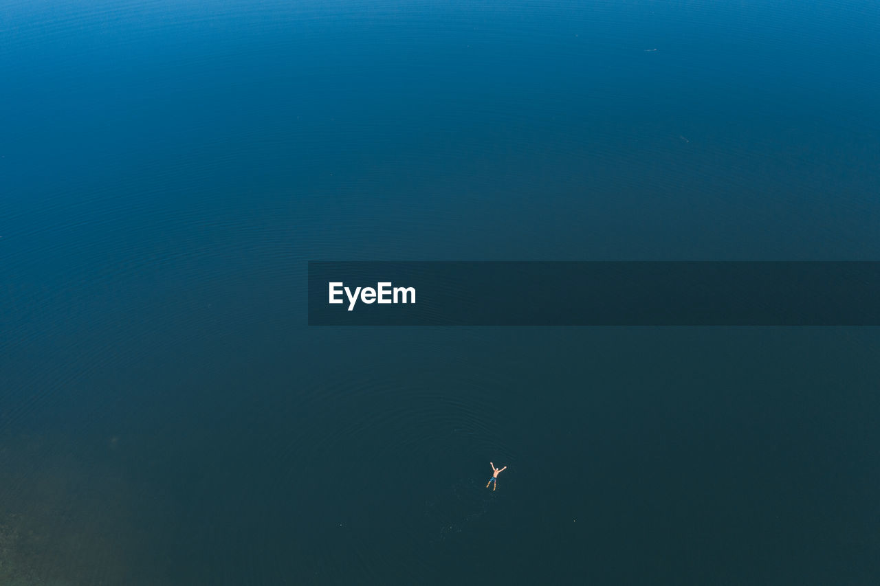 Man rest on sea waters, lie with legs and hands stretched out, top-down aerial shot. 