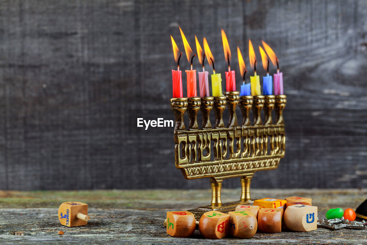 Toy blocks by colorful candles burning on wooden table