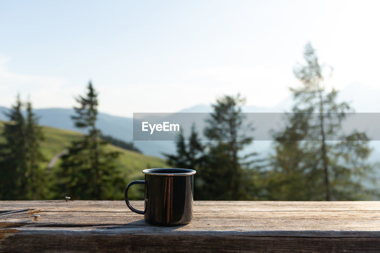Tin mug on the wooden bench on the mountains background. hiking concept