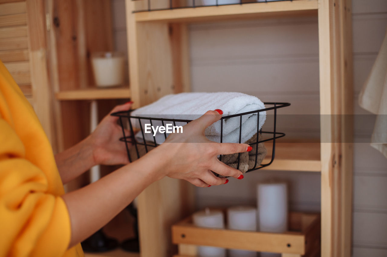 A young woman at home cleans a basket with towels in the closet on the shelf