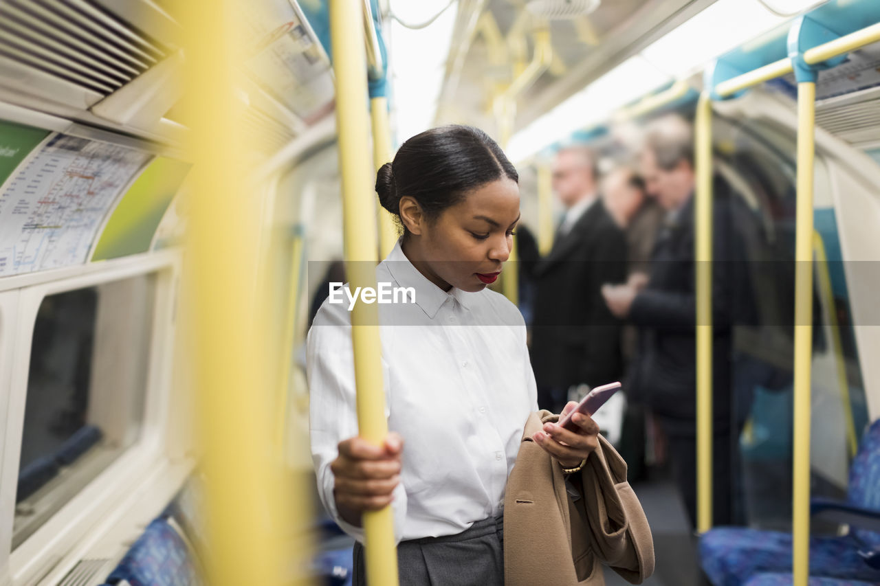 Uk, london, businesswoman in underground train looking at cell phone