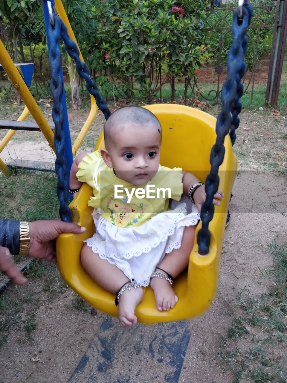 Cropped hand of man by girl sitting on swing