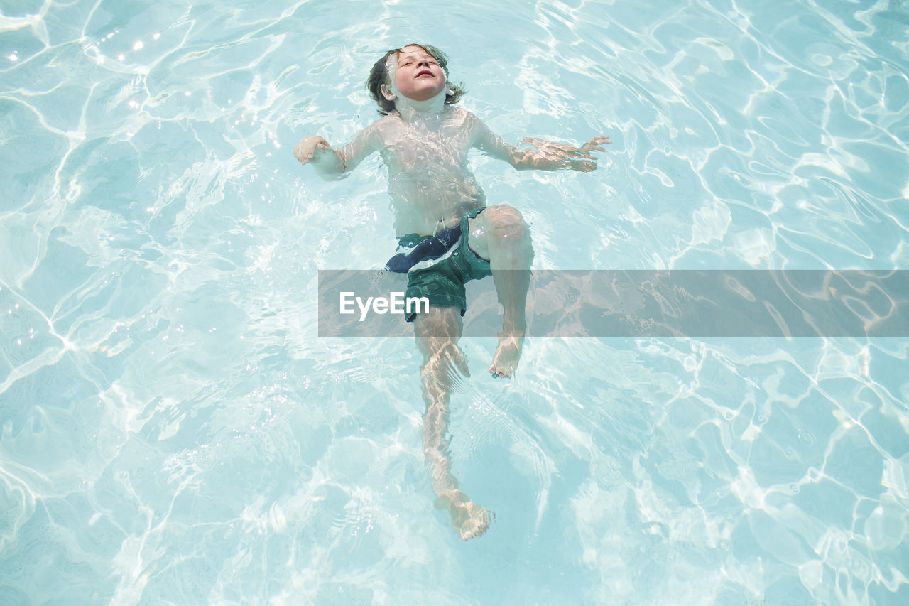 Young boy swims on back submerged in pool with face in the sun