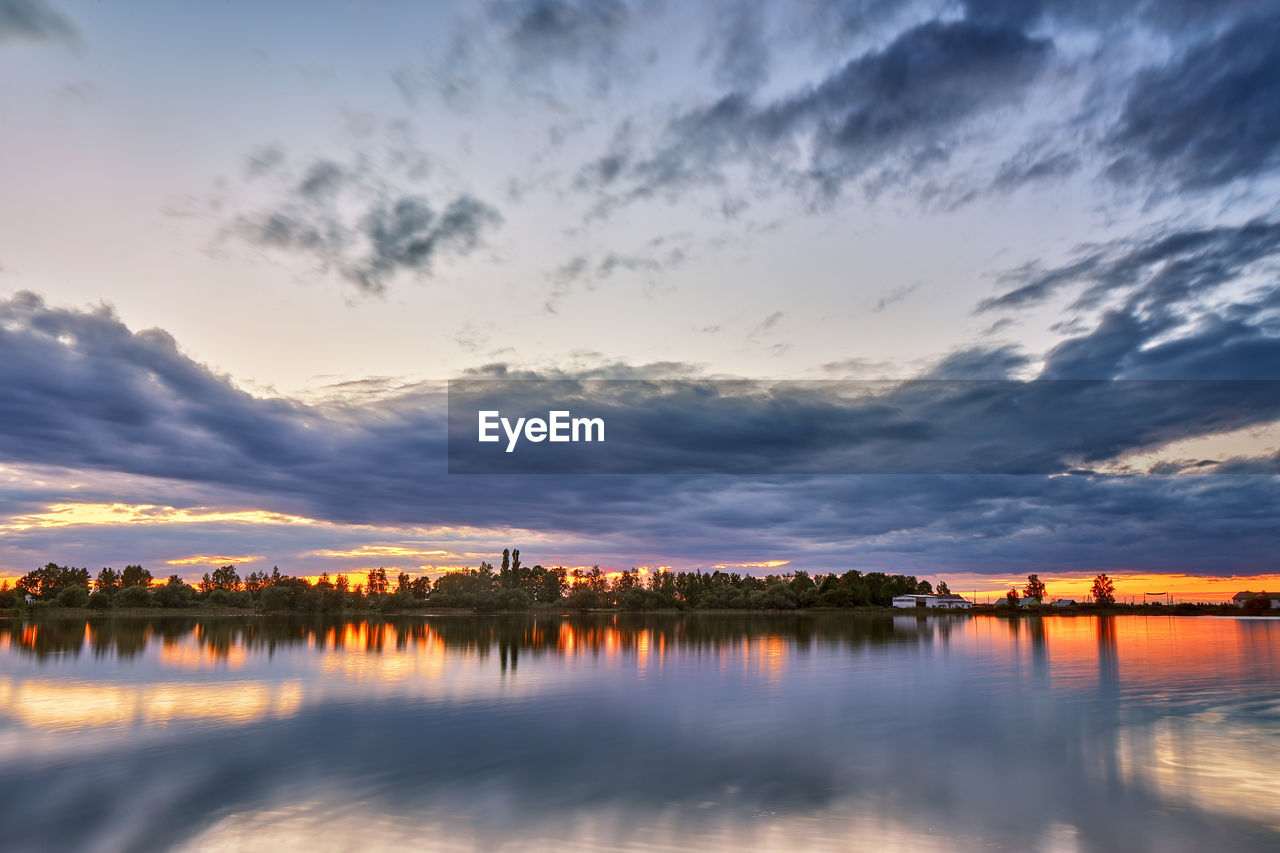 Summer sunset on lake. village on lakeside. dusk rural scene. storm cloudscape, rainy weather.